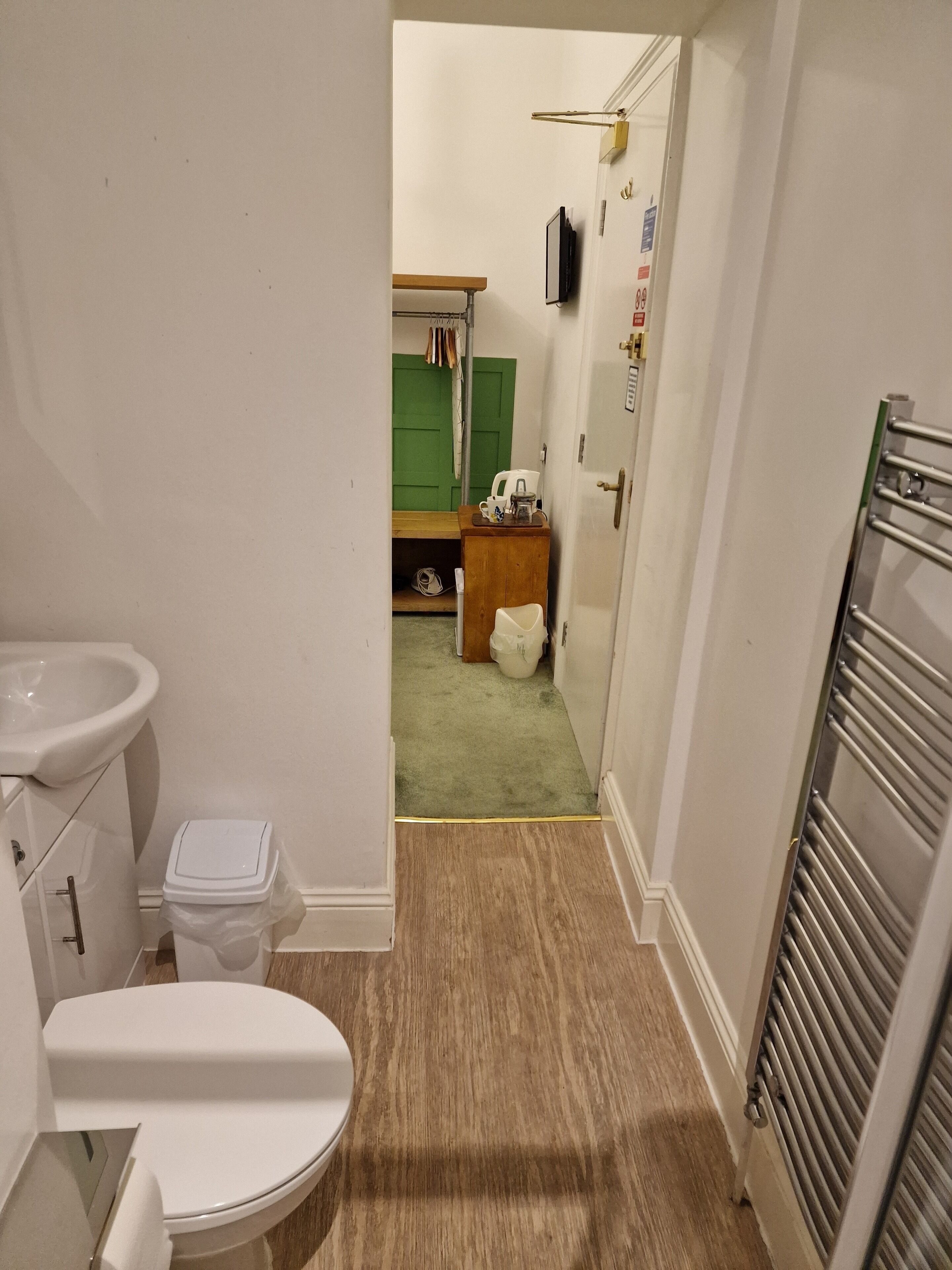 Un pasillo estrecho que conduce a un cuarto de baño con inodoro, lavamanos y una puerta verde.
