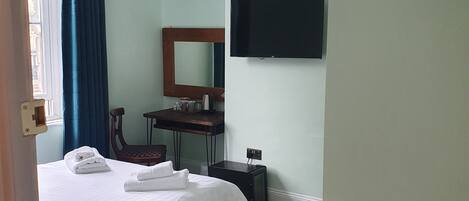 A hotel room with a bed, a desk, a chair, a television, and a small table.