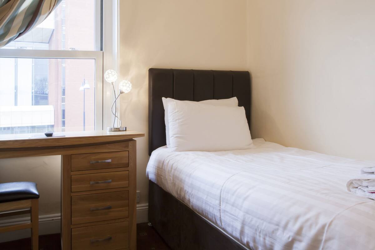 A bedroom with a bed, a wooden desk, and a window with curtains.
