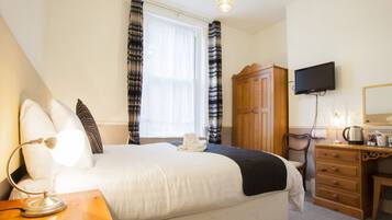 A hotel room with a large bed, a wooden dresser, a television mounted on the wall, and a window with curtains.