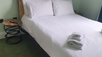 A neatly made bed with white linens, a wooden headboard, and two wall-mounted light fixtures.