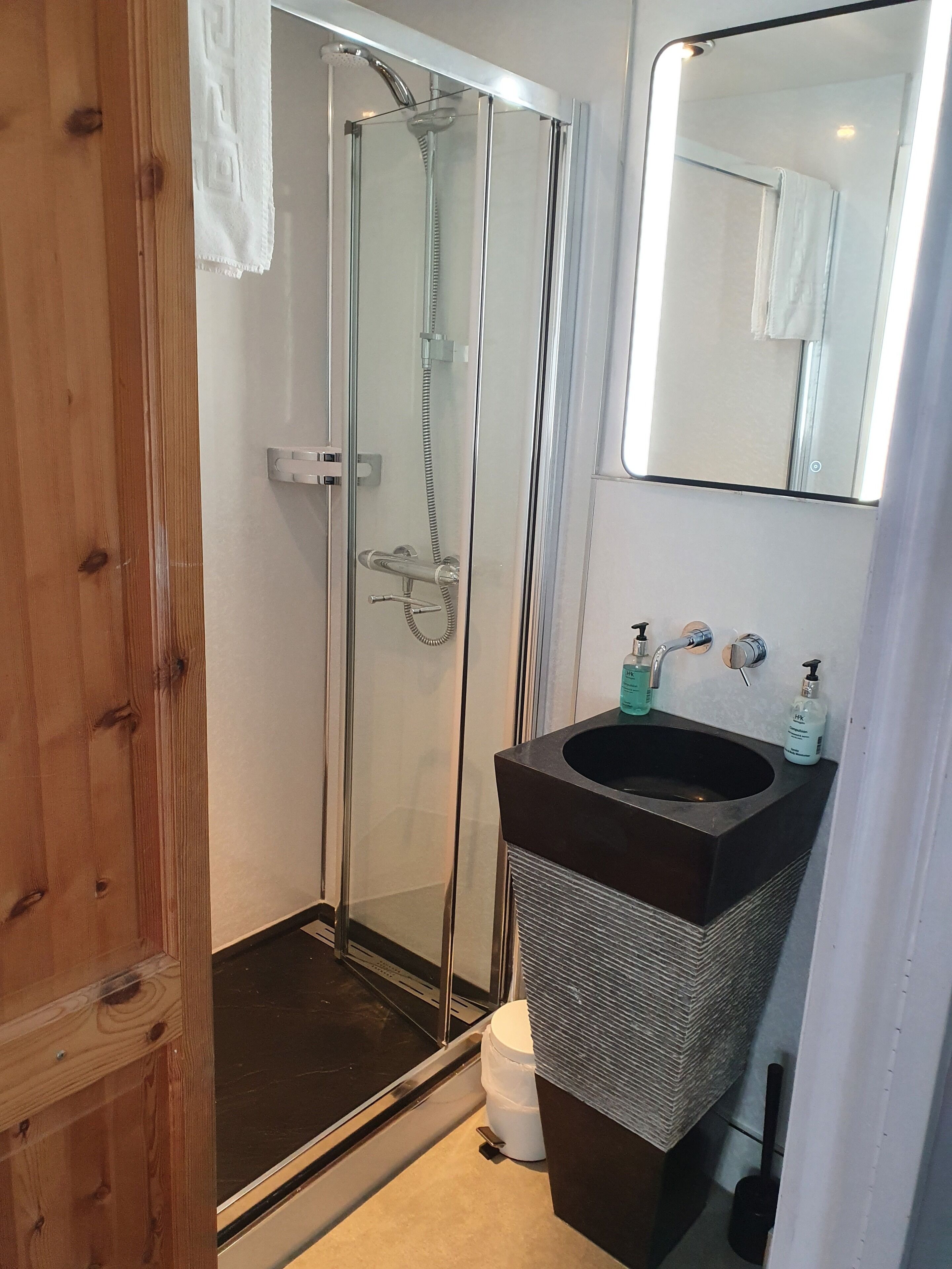 Un baño con ducha de vidrio, un lavamanos con encimera oscura y un espejo sobre el lavamanos.