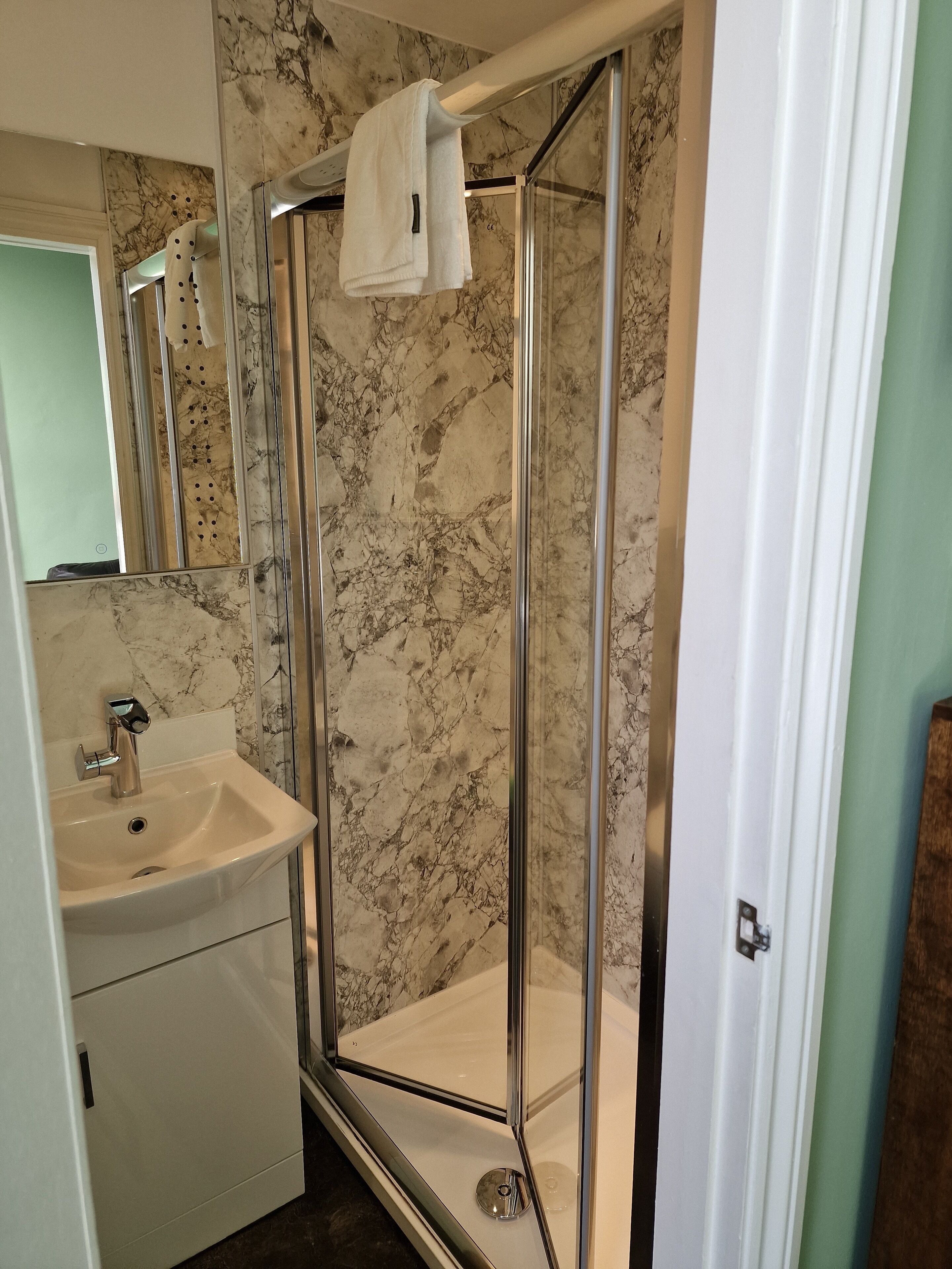 A bathroom with a glass-enclosed shower, a sink, and a marble backsplash.