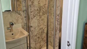 A bathroom with a glass-enclosed shower, a sink, and a marble backsplash.