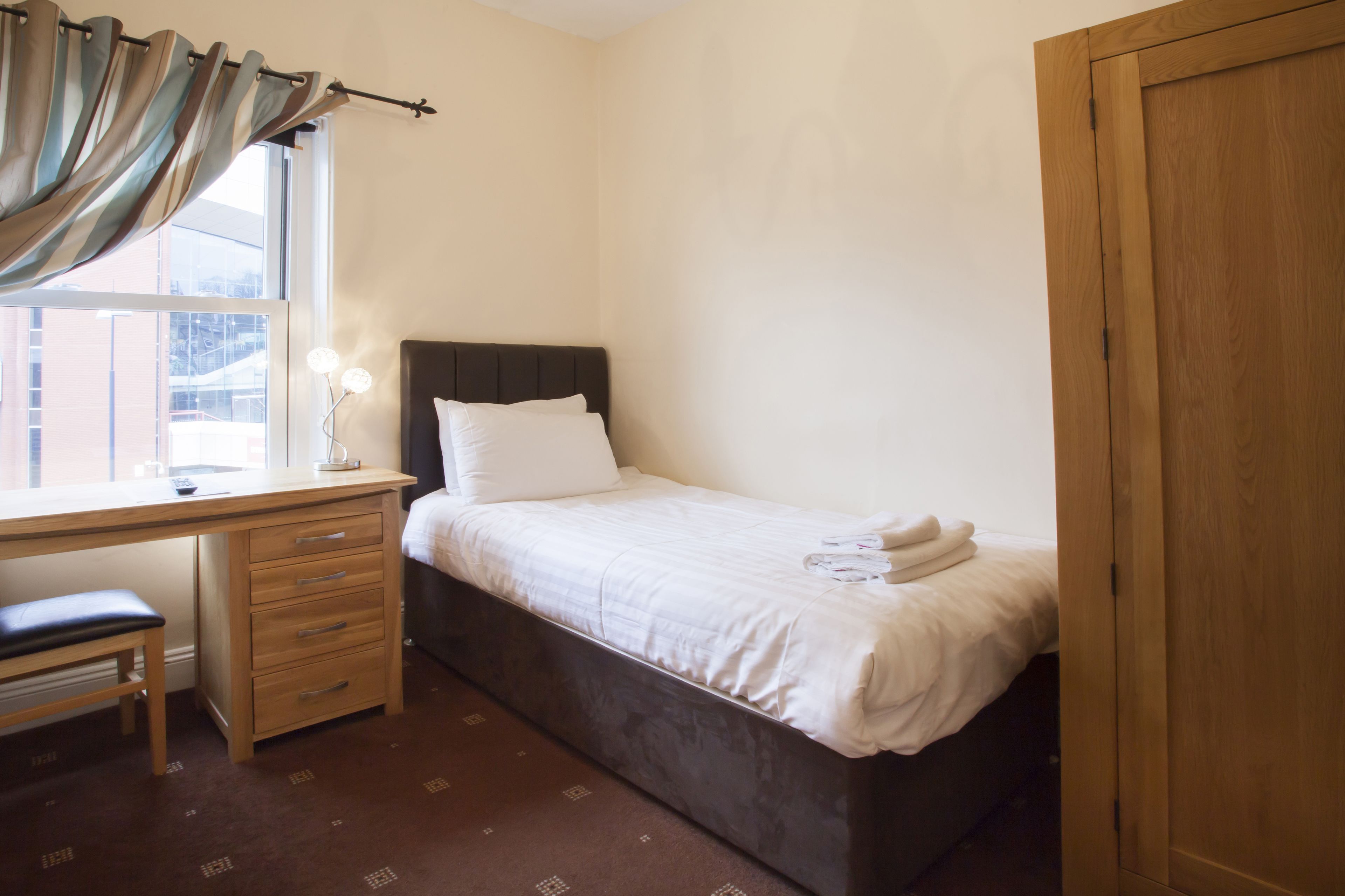 A bedroom with a single bed, a wooden desk, a chair, and a wardrobe.