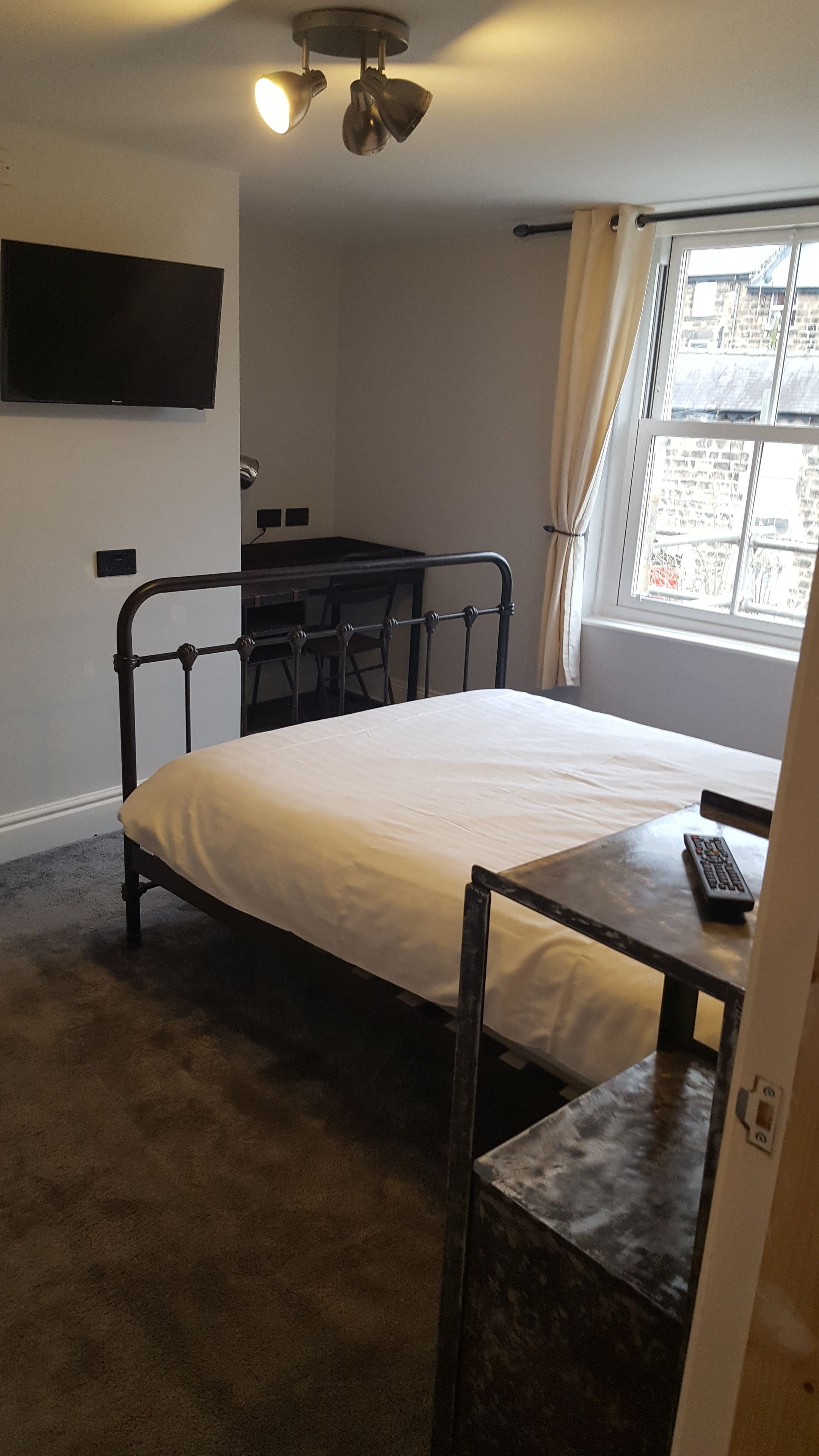 A room with a bed, a desk, a chair, a TV, and a window with curtains.