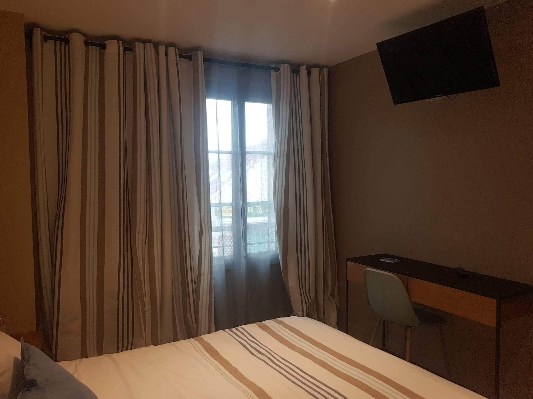 Una habitación de hotel con una cama, un escritorio y un televisor montado en la pared.