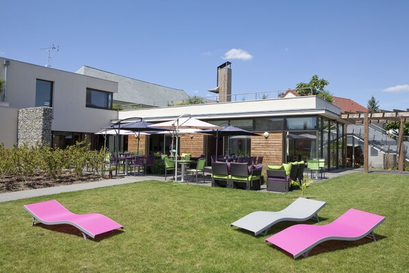 A modern outdoor seating area with lounge chairs and tables, a stone wall, and a clear sky.