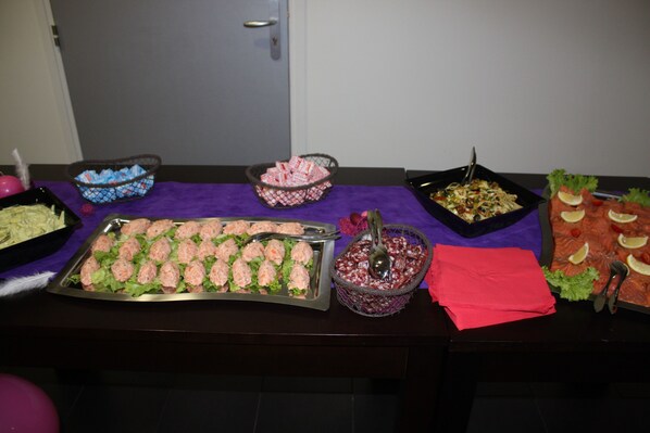 A buffet table with various food items including meatballs, salad, and salmon, arranged on a purple tablecloth.