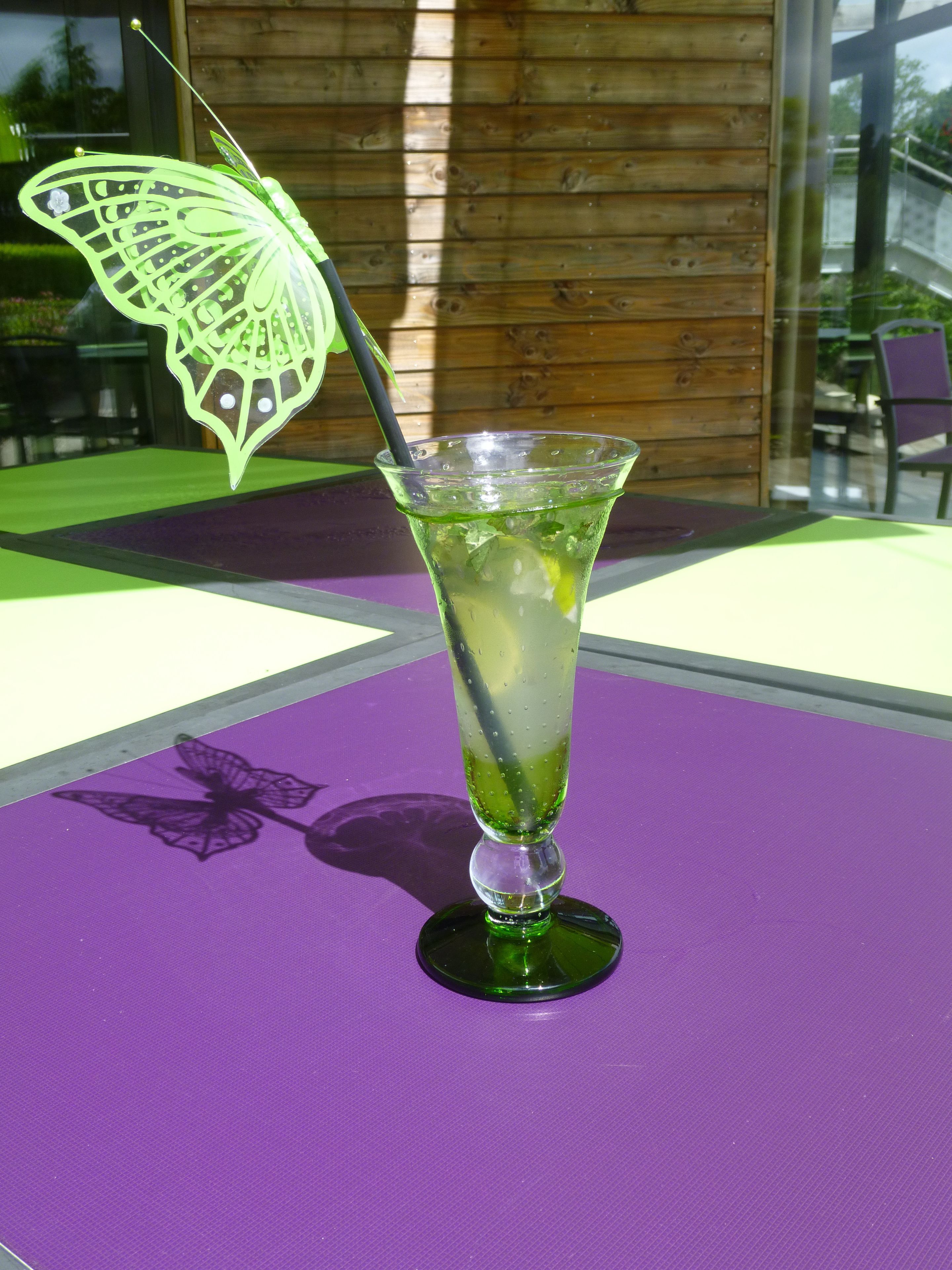 Ein Cocktailglas mit einer grünen Schmetterlingsdekoration auf einer violetten Tischdecke.