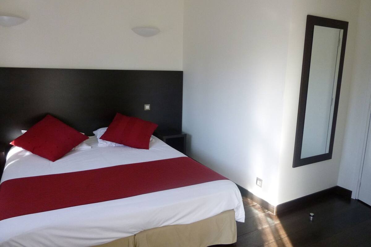 A hotel room with a bed, a nightstand, a mirror, and a window.