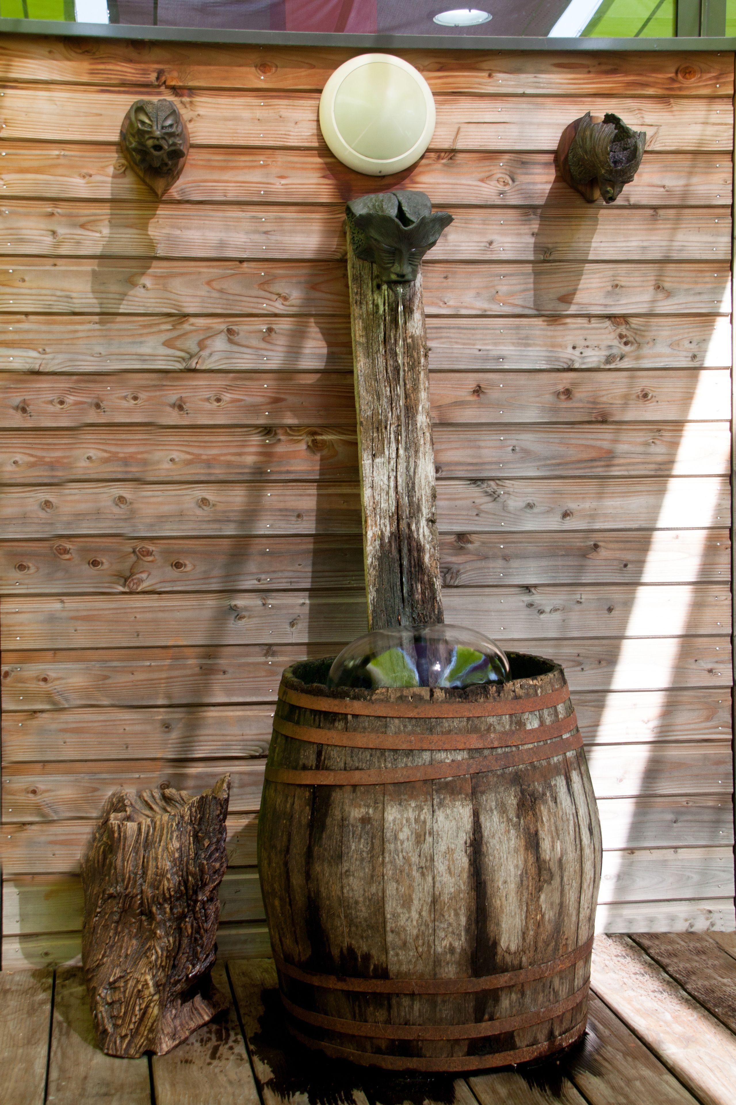 Une fontaine rustique en forme de tonneau en bois, agrémentée d’un panneau de fond en bois et d’éléments décoratifs.