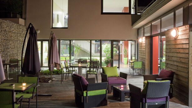 An outdoor patio area with wicker furniture, green chairs, and a stone wall.