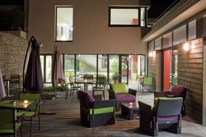 An outdoor patio area with wicker furniture, green chairs, and a stone wall.