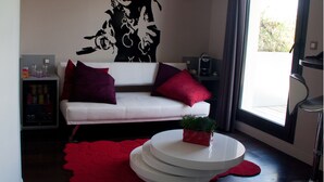 A modern living room with a white sofa, red cushions, a coffee machine, and a large window with curtains.