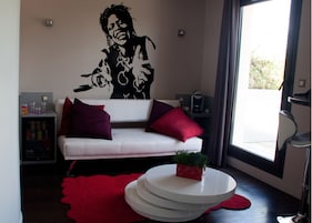 Una sala de estar moderna con un sofá blanco, cojines rojos, una cafetera y un amplio ventanal con cortinas.