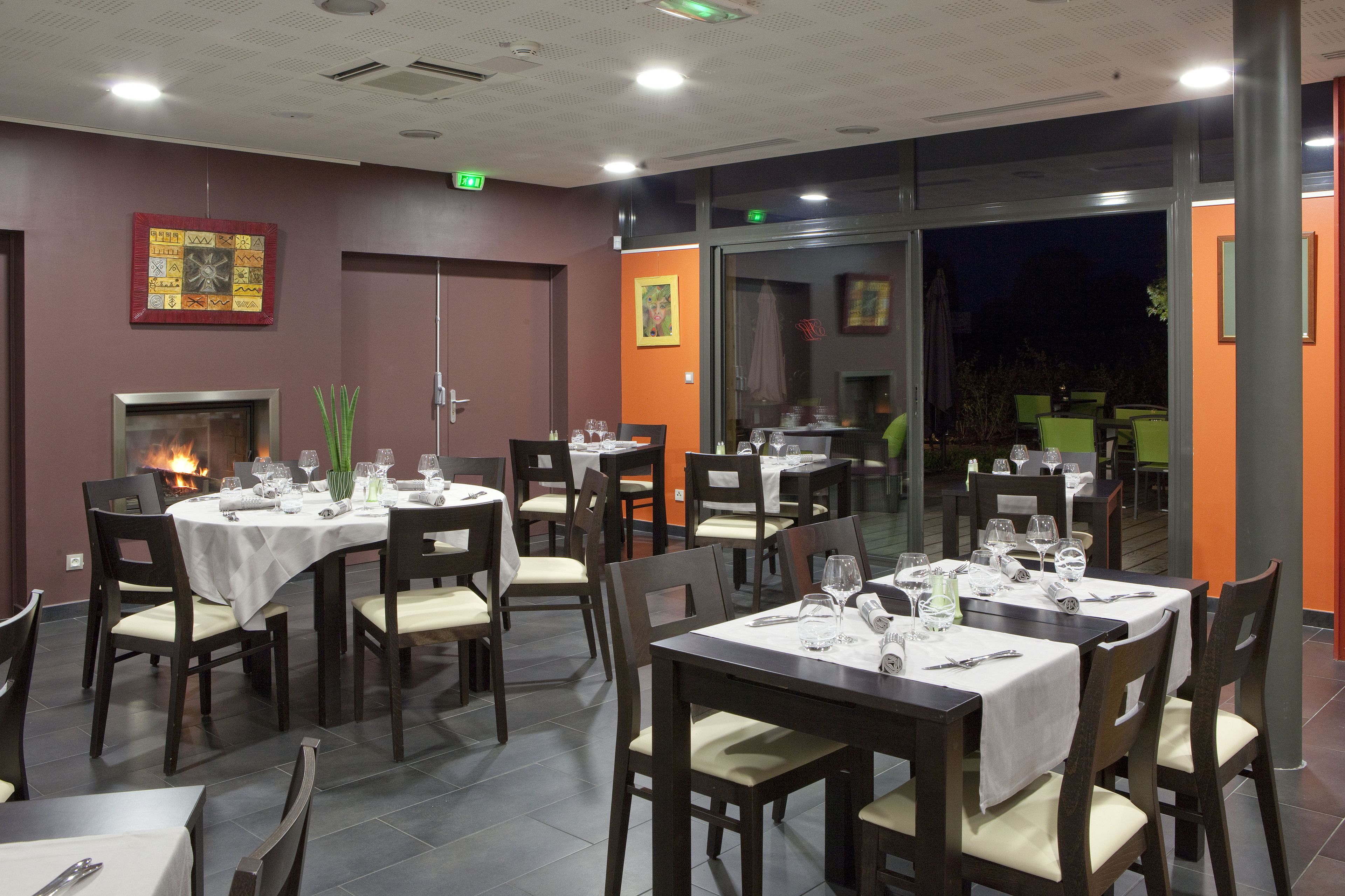 Un restaurante con varias mesas dispuestas para comer, una chimenea y amplias ventanas con vistas al exterior.