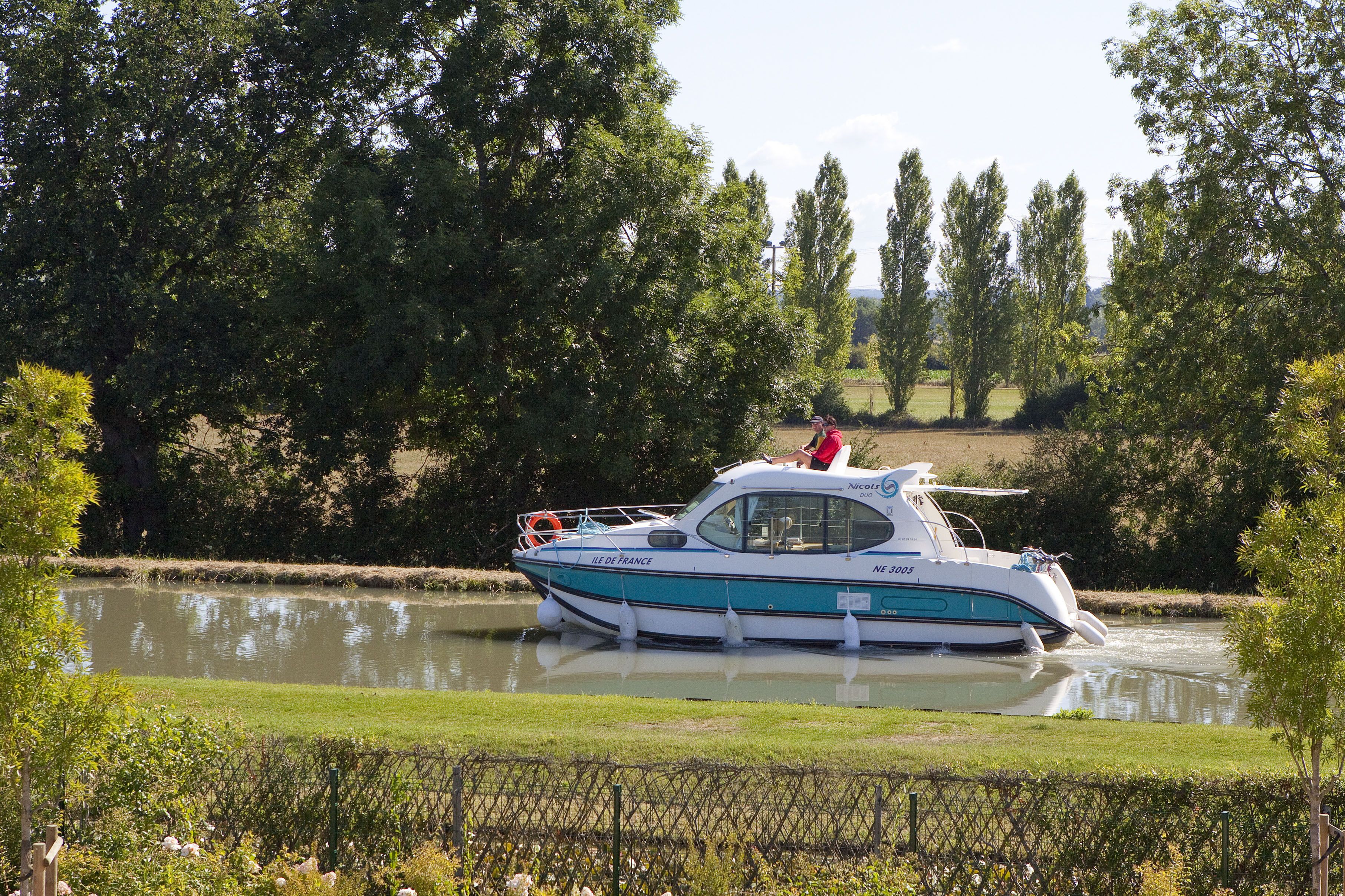 A boat named "Île de France" on a calm river surrounded by greenery.