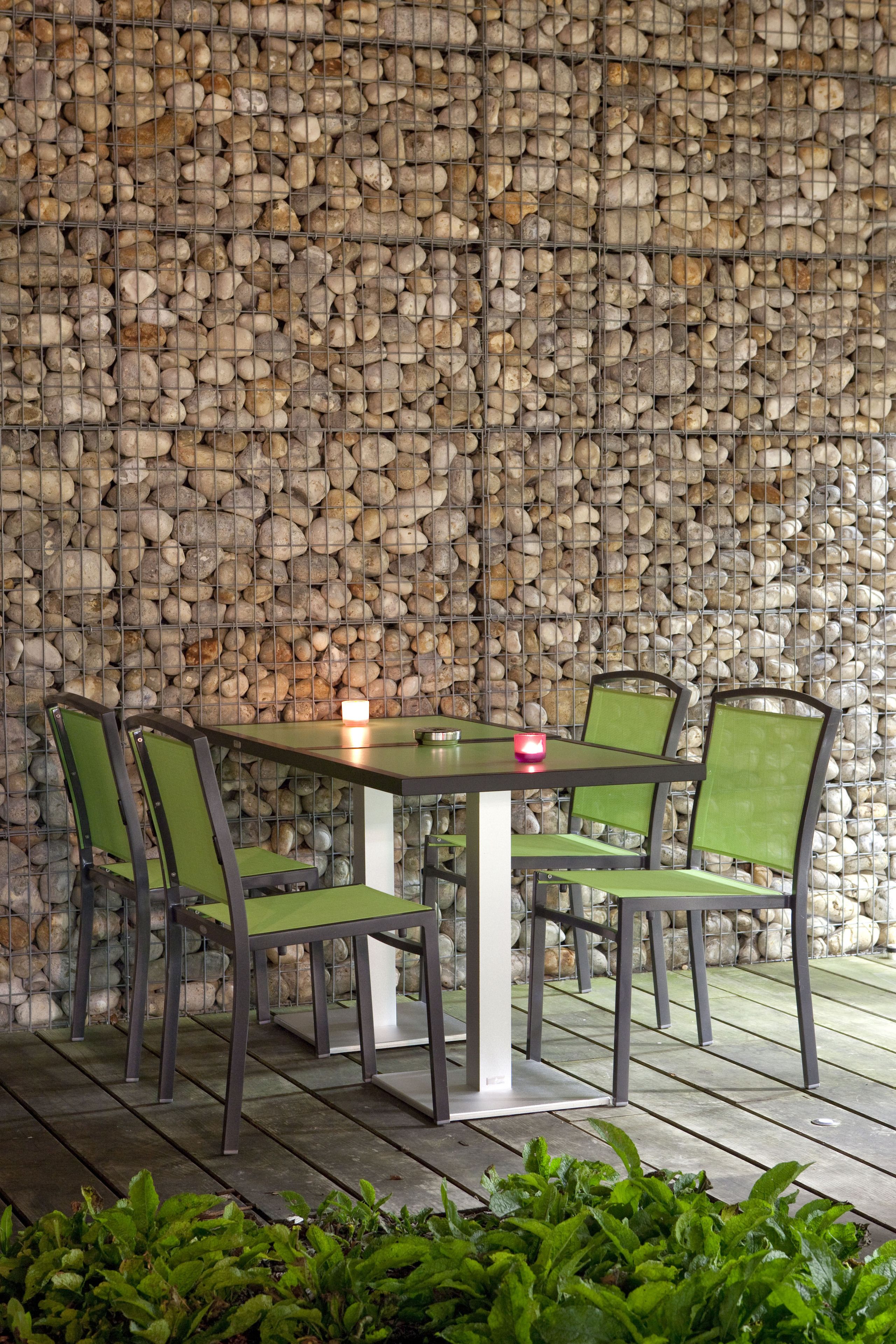 A table and chairs set against a wall of stacked stones, with a candle on the table.