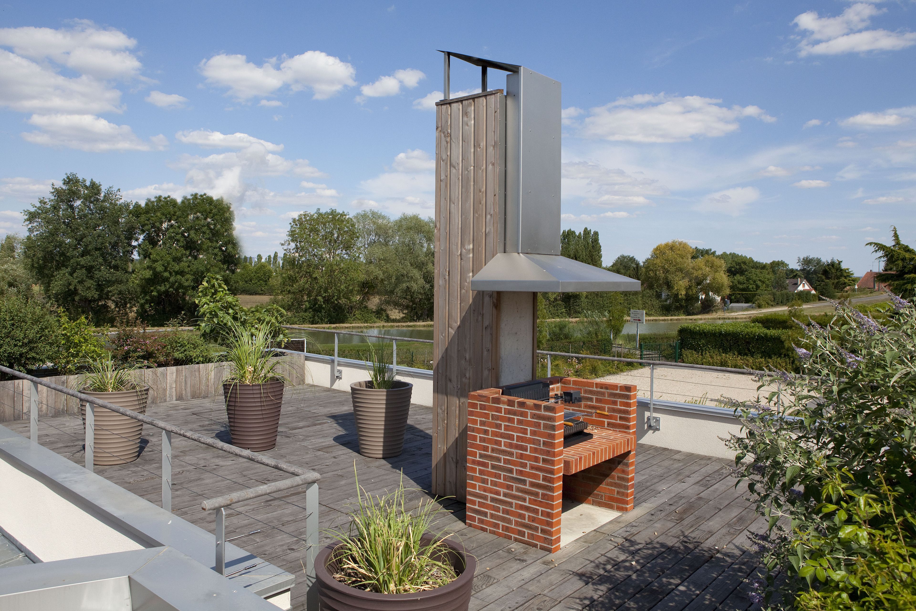A rooftop patio with a brick barbecue, potted plants, and a wooden pergola structure.