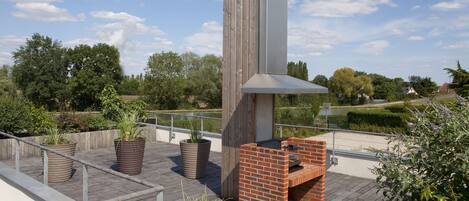 A rooftop patio with a brick barbecue, potted plants, and a wooden pergola structure.