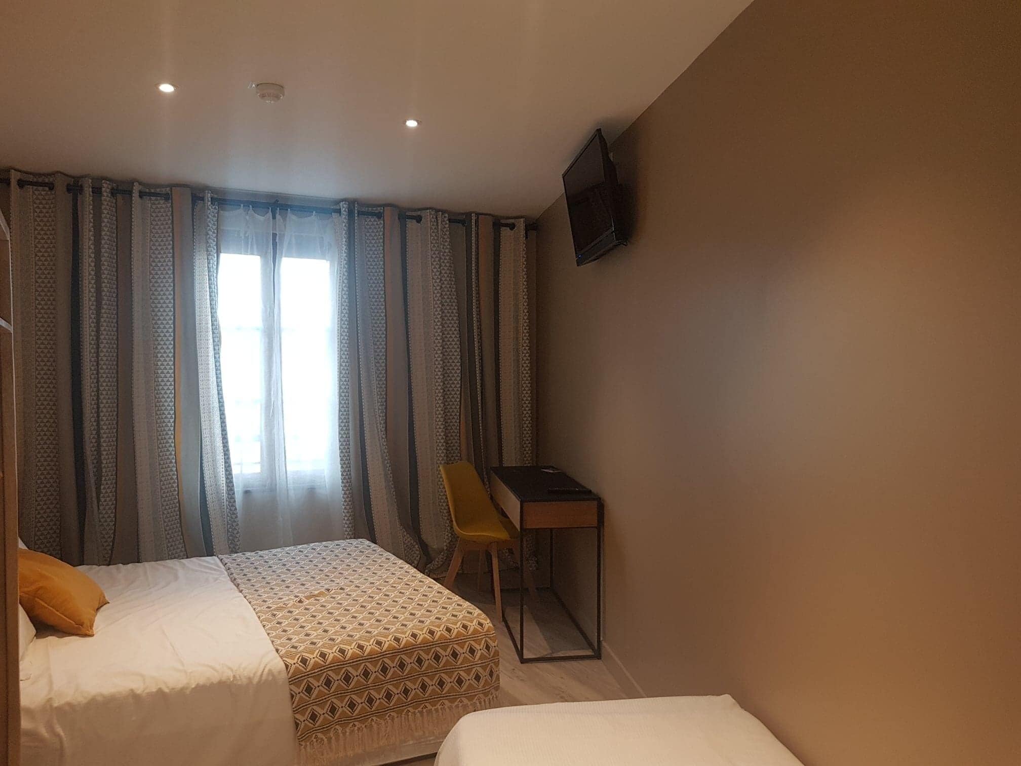 A hotel room with two beds, a desk, and a TV on the wall.