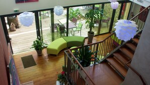 A multi-level interior with wooden flooring, a staircase, and a balcony area with outdoor seating and potted plants.
