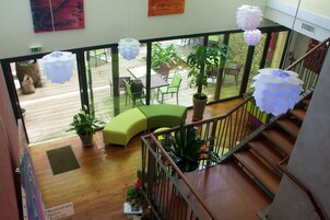 A multi-level interior with wooden flooring, a staircase, and a balcony area with outdoor seating and potted plants.
