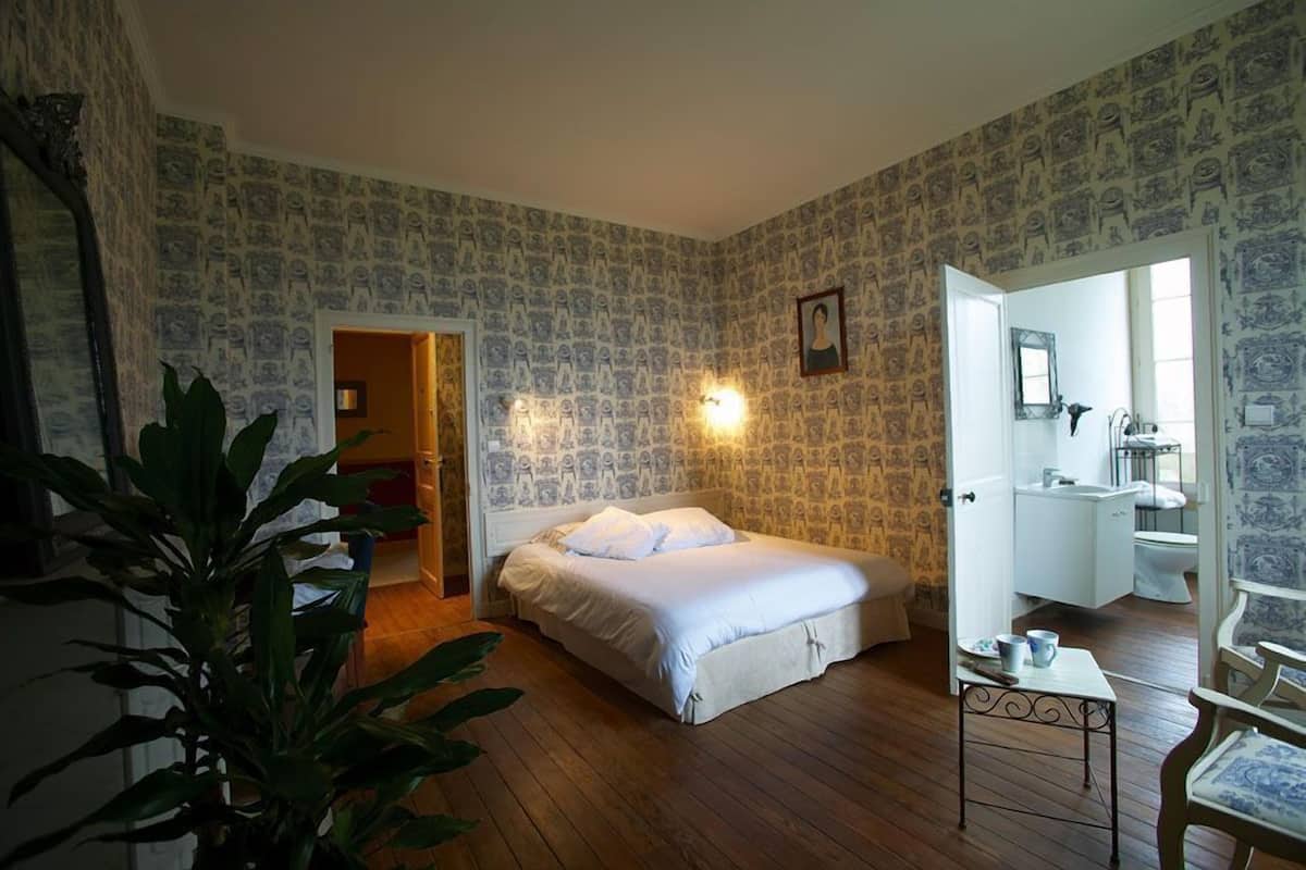 A bedroom with a bed, a bedside table, a mirror, and a door leading to a bathroom.