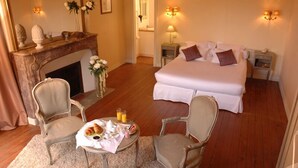A hotel room with a large bed, two bedside tables, a fireplace, a sitting area with a table and chairs, and a mirror. - Domaine de Bel Air (Cerans-Foulletourte)