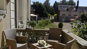 A patio with wicker furniture, a small table with a vase of flowers, and a patterned floor. - Domaine de Bel Air (Cerans-Foulletourte)
