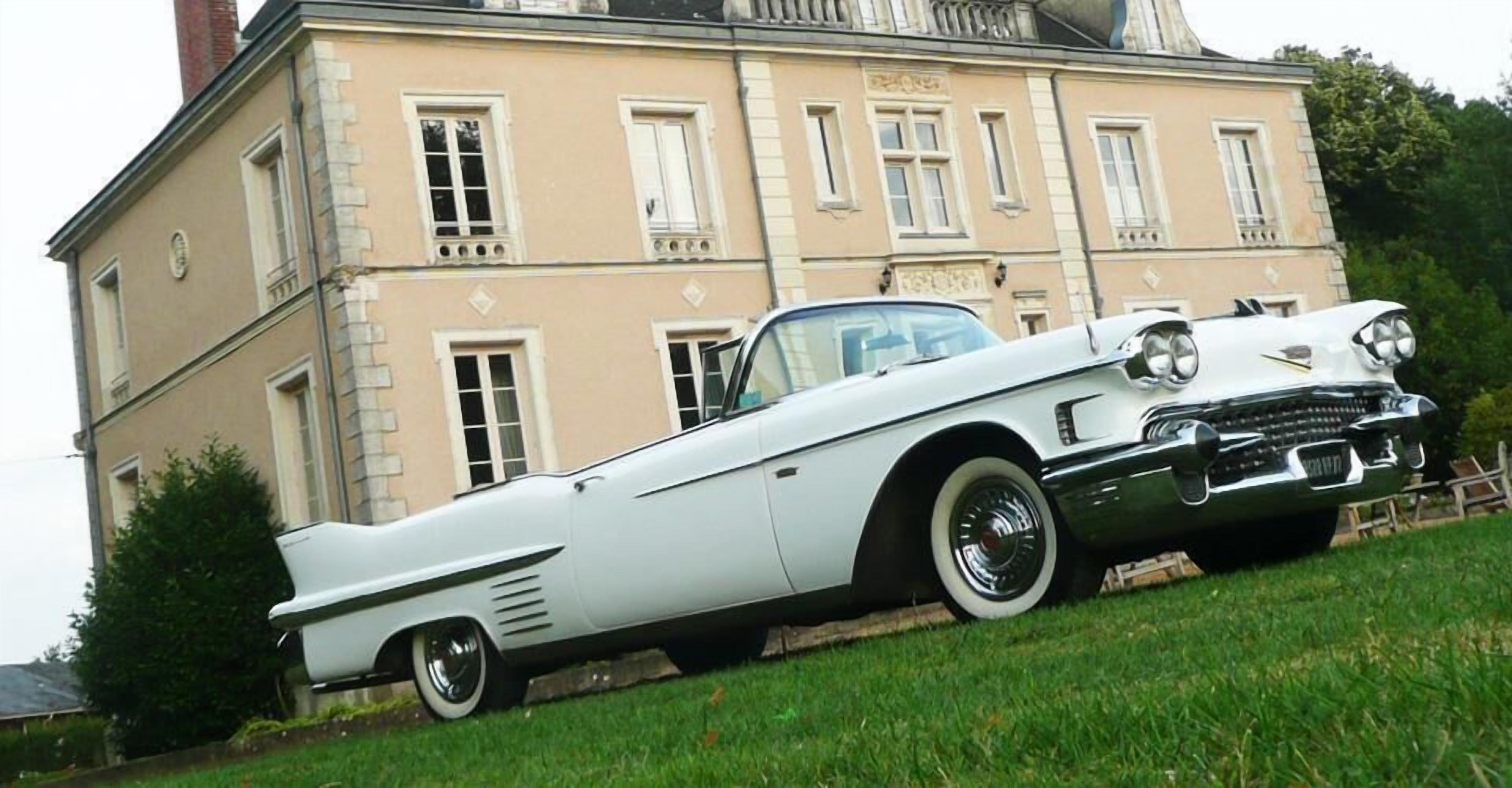 A classic white convertible car parked in front of a large, multi-story building with a symmetrical facade and evenly spaced windows.