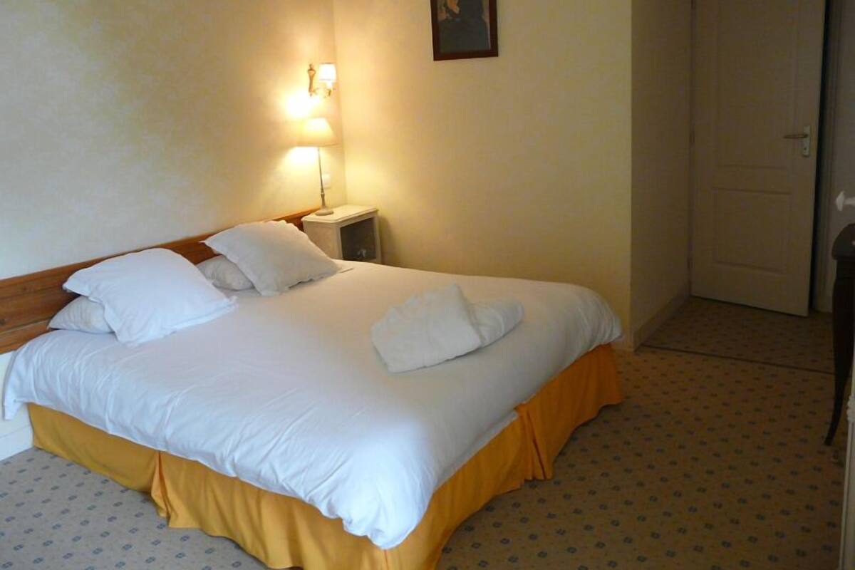 A neatly made bed with white linens and a yellow skirt, a bedside lamp, and a framed picture on the wall.