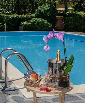 Una mesa junto a la piscina con una botella de champán, copas, una flor y un adorno.