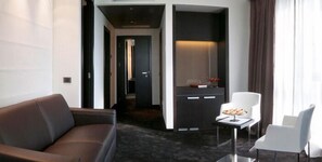 A modern hotel room with a dark carpet, a brown leather sofa, a white armchair, and a small table with a plate of food. - Parco dei Principi Hotel Congress & Spa (Bari)