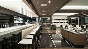 A modern bar area with a long counter, bar stools, and a well-lit ceiling.