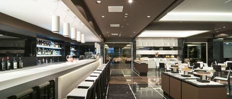 A modern bar area with a long counter, bar stools, and a well-lit ceiling.