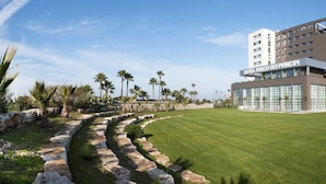 A modern hotel with a central courtyard, palm trees, and a clear sky.