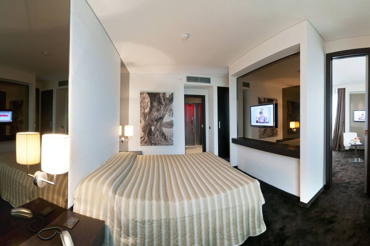 A hotel room with a large bed, bedside lamps, a television, and a mirror.