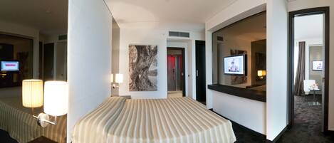 Una habitación de hotel con una cama grande, lámparas de noche, televisión y espejo.