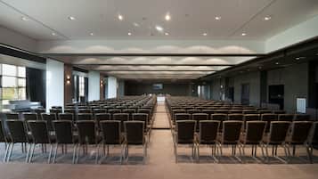 Un salón de conferencias con filas de sillas, una pantalla grande al frente y un diseño moderno del techo.