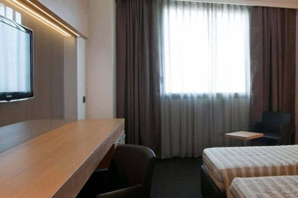 A hotel room with a bed, a desk, a chair, a TV, and a window with curtains.