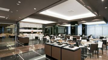 A modern hotel lobby with a central island, seating areas, and a kitchen in the background.