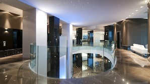A modern hotel lobby with a glass railing, a curved staircase, and a white reception desk.