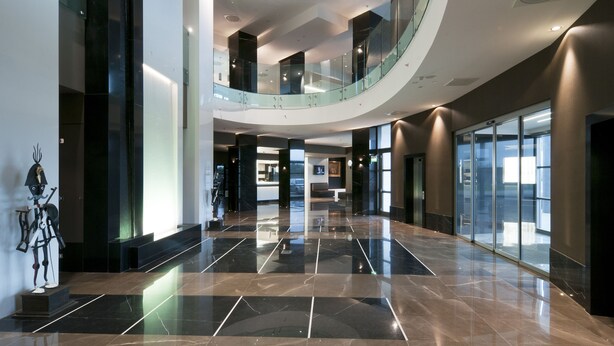 A spacious lobby with a curved glass railing, polished marble floors, and a statue on the left.
