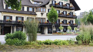 A hotel with multiple balconies adorned with flowers, a prominent sign, and a cobblestone street in front. - Hotel Adler - Post (Baiersbronn)