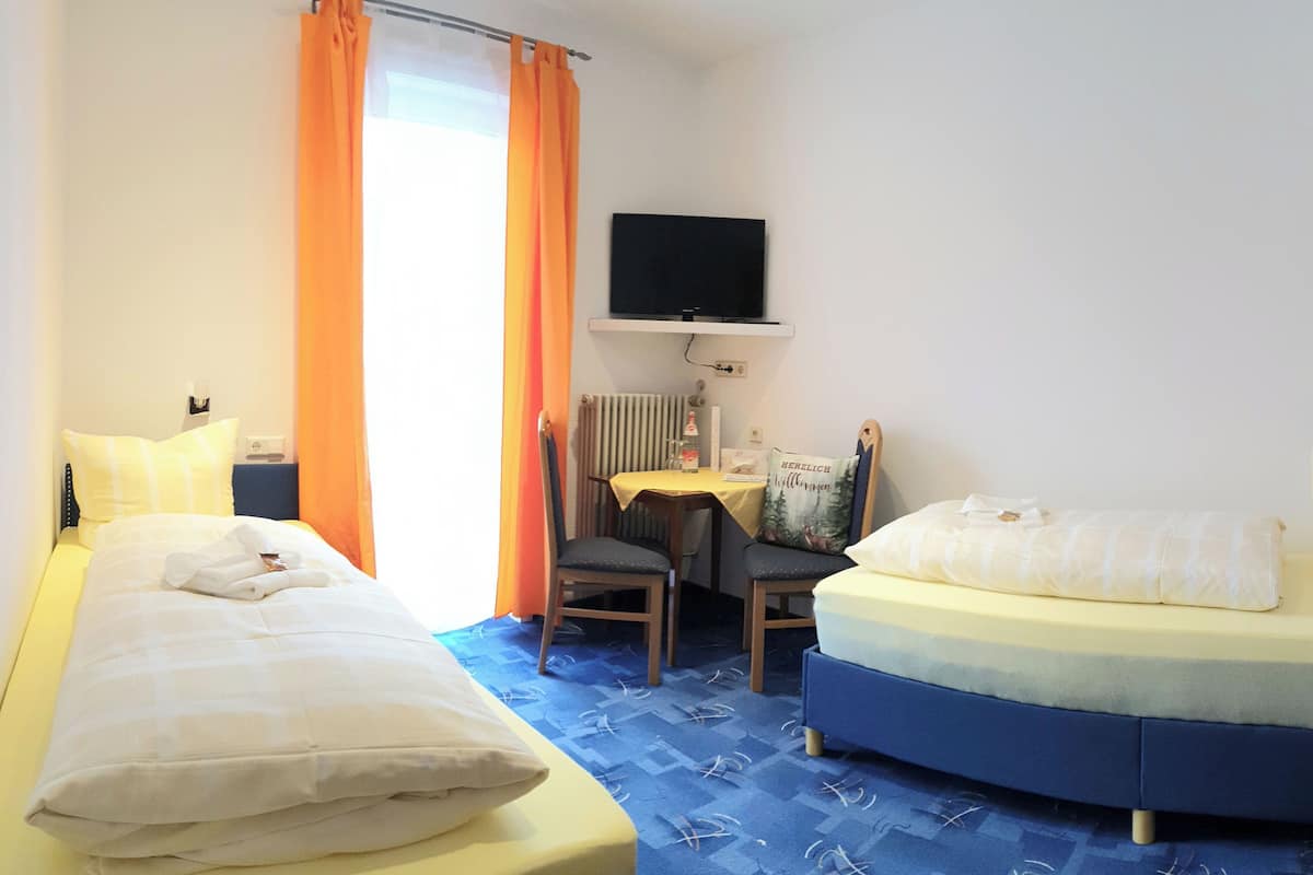 A hotel room with two beds, a desk with a chair, a television, and a radiator.