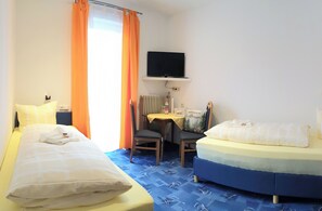 A hotel room with two beds, a desk with a chair, a television, and a radiator. - Hotel Adler - Post (Baiersbronn)