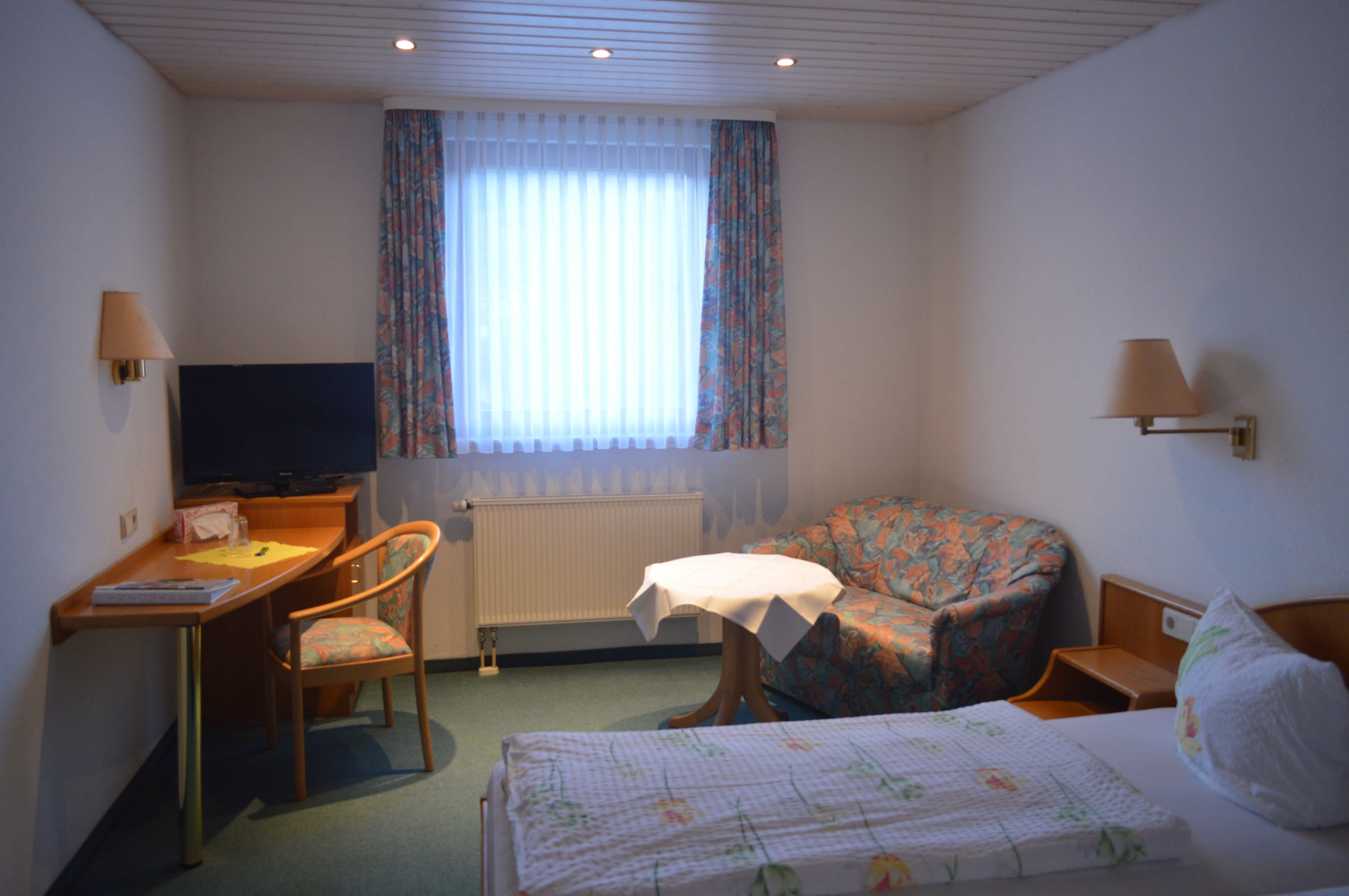 A hotel room with a bed, a desk, a chair, a television, and a window with curtains.