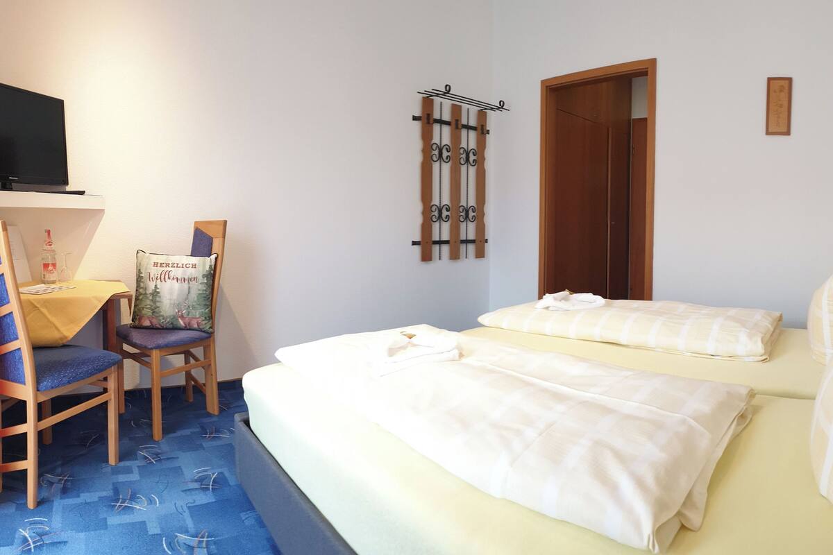 A hotel room with two beds, a desk with a chair, a television, and a wall-mounted rack.